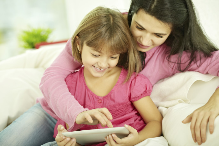 Mother with daughter siting on sofa at home and playing with digital tablet pc together