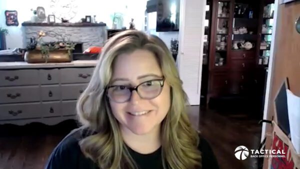 A woman with long, wavy blonde hair and glasses is smiling. She is sitting in a room with a wooden cabinet and a white dresser in the background. A "Tactical Back Office Personnel" logo is visible in the bottom right corner.