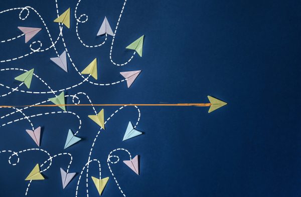 Several pastel-colored paper airplanes fly in various directions with dashed lines on a blue background. One yellow paper airplane flies straight to the right, marked by an orange solid line.
