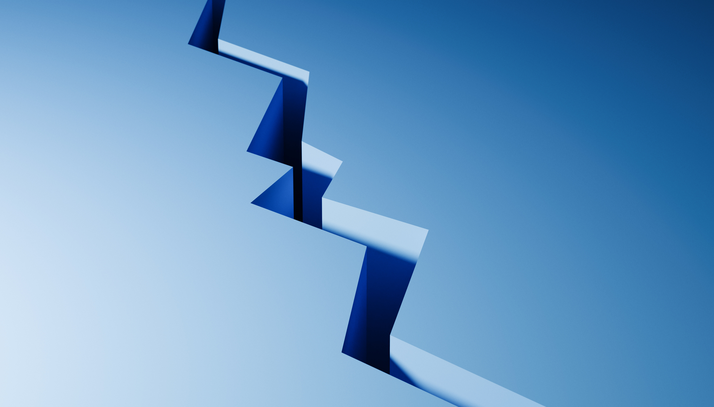 A jagged, zigzag crack runs diagonally across a smooth blue surface, casting sharp shadows and creating a stark contrast between the split sections.