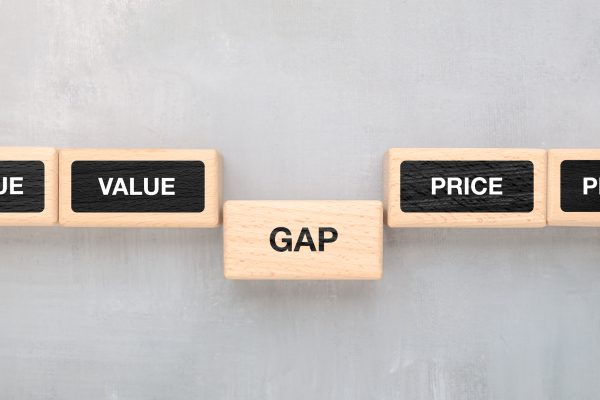 Wooden blocks form a row on a light-colored surface. The blocks display the words “VALUE,” “GAP,” and “PRICE,” with “GAP” positioned between “VALUE” and “PRICE.”.